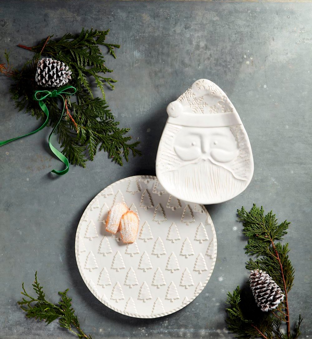 2 styles of white christmas platters arranged on a grey surface with greenery and ribbons.