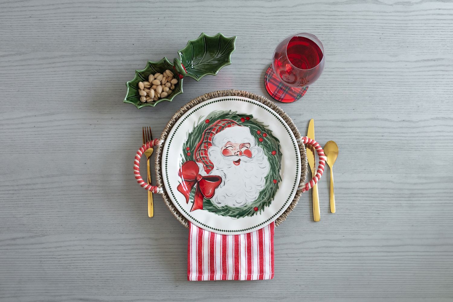 top view of a table set with a santa platter in a seagrass basket with gold silverware and a glass of wine.