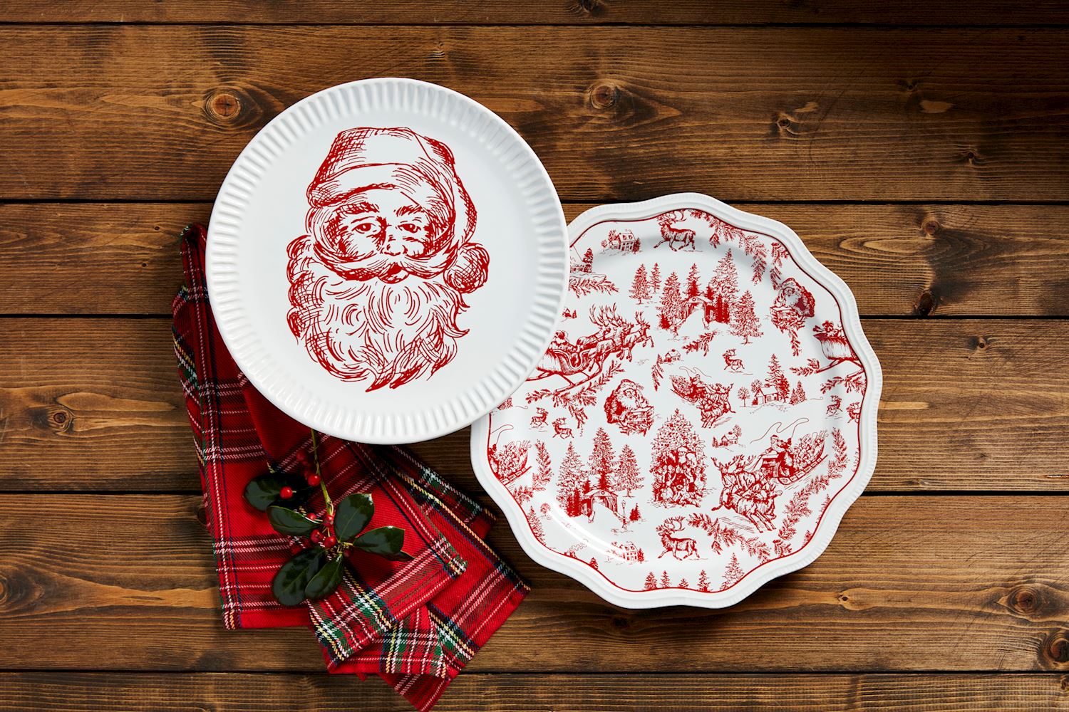 2 styles of christmas platters arranged on a wooden table with tartan napkins and a sprig of holly.