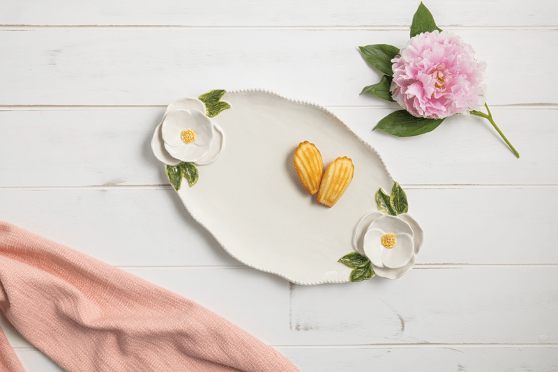 white platter with beaded rim and white flowers on each end and cookie on it set on a wooden table with linens and a pink flower