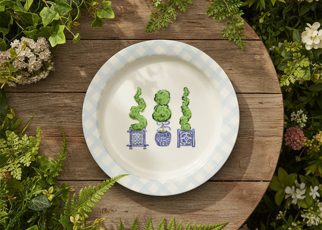 round platter with blue gingham boarder with 3 topiary drawings in the center set on a table surrounded by greenry