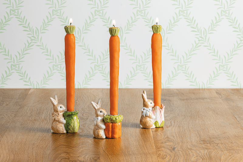 Three taper candle holders with rabbit figures on a wooden surface and patterned wall background.