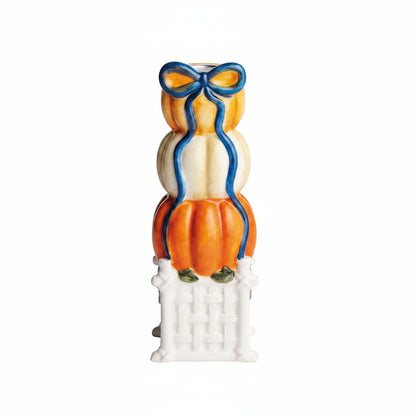 large pumpkin topiary taper holder designed as a stack of three pumpkins, 2 orange, the middle pumpkin is white, white a blue bow painted at top and stack sits on a white pedestal