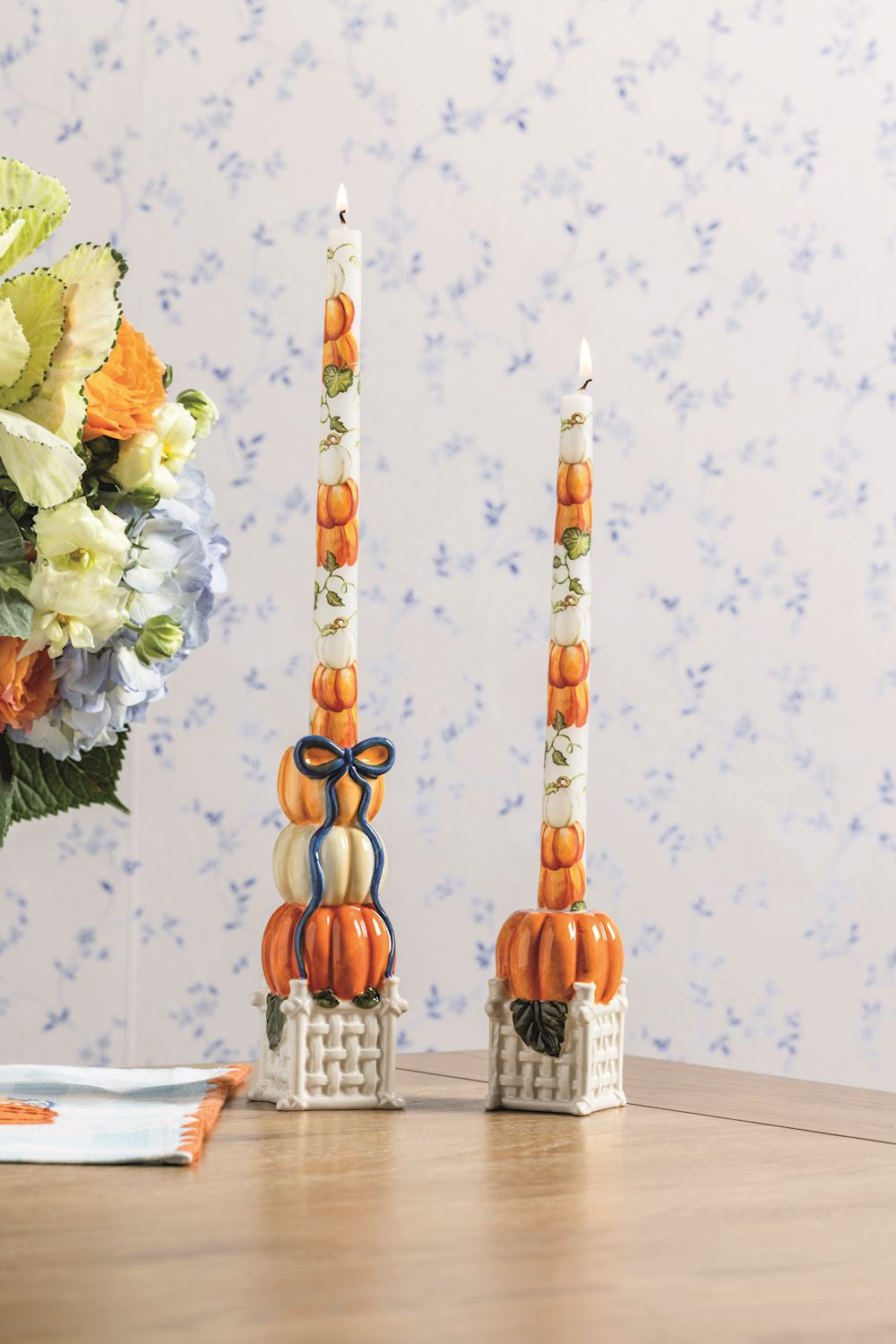 2 pumpkin topiary taper holders with tapers in them on a table with a floral arrangement
