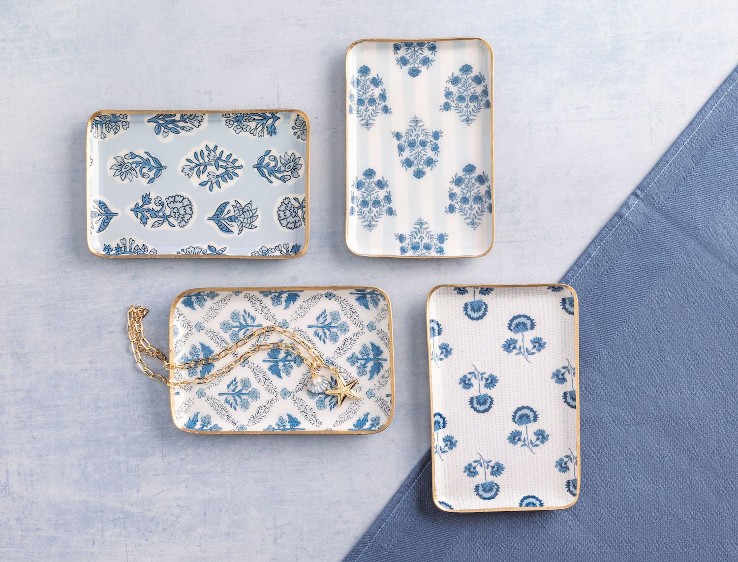 four assorted decorative metal trays with blue floral patterns on a light gray surface.