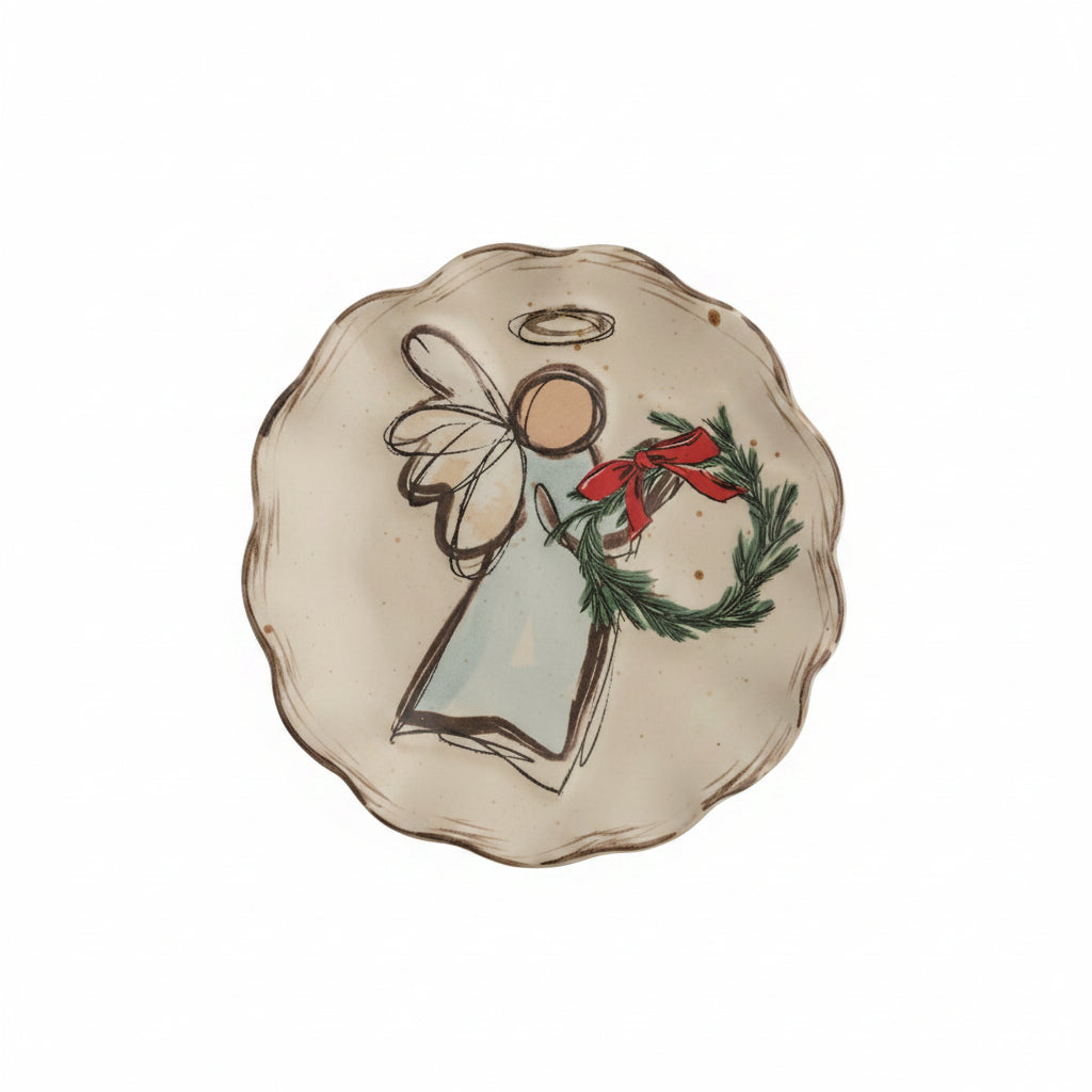A scalloped ceramic plate with a hand-painted angel holding a green wreath with a red bow shown on a white background.