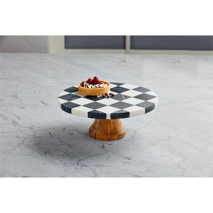 black and white check marble cake plate with a mango wood pedestal on a stone countertop with a fruit tart set on the pedestal.