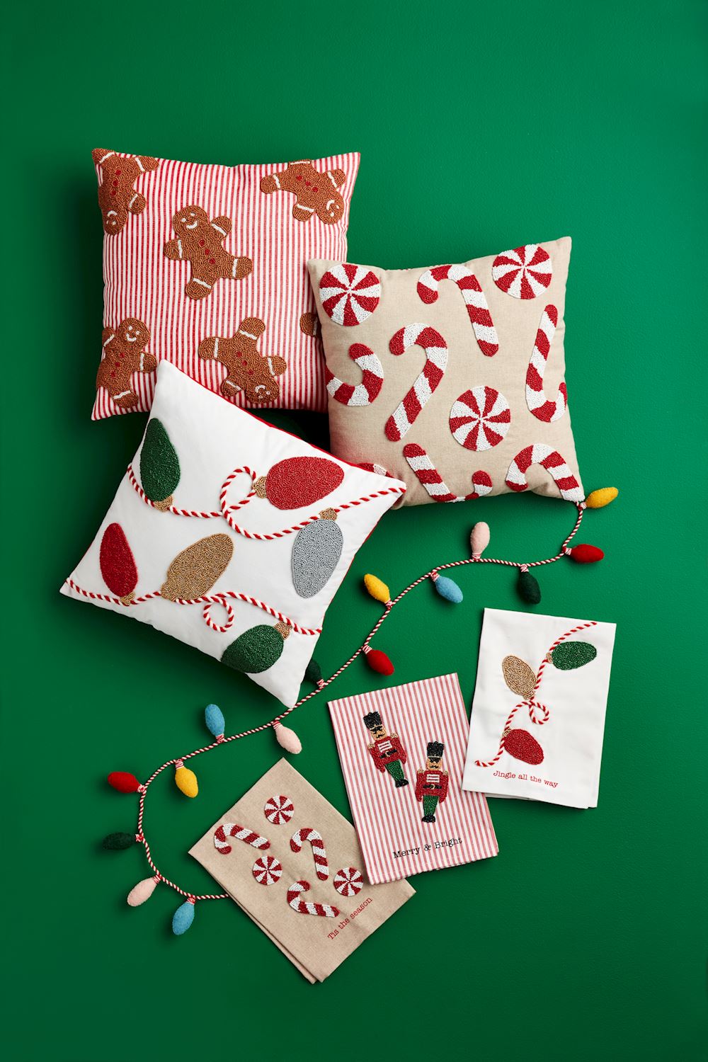 3 assorted Beaded Christmas Pillows arranged on a green background with christmas lights and towels.