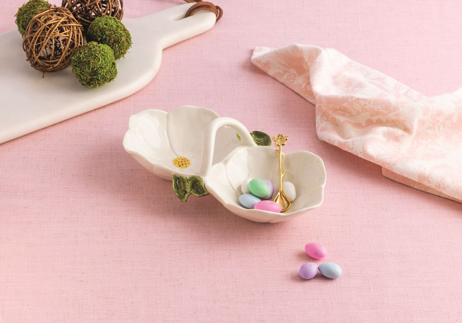 flower double tidbit bowl, one side filled with pastel candles, set on a pink tablecloth with linens and decorative items