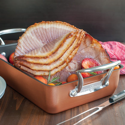 copper roaster filled with sliced ham and veg on a table with a meat fork.