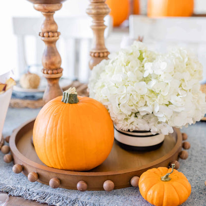 round wooden tray with beads around the rim arranged on a table with flowers and pumpkins.