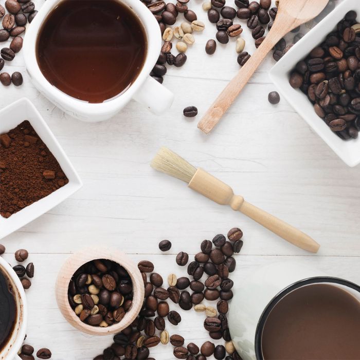 Coffee beans, cups of coffee, and a Coffee Grinder Brush on a white wooden surface