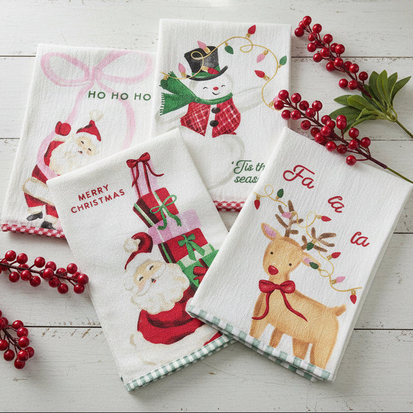 4 assorted whimsical christmas tea towels arranged on a white table with red berries