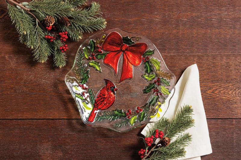  glass plate with a cardinal and bow on a wreath design painted on it on a wooden surface with evergreens