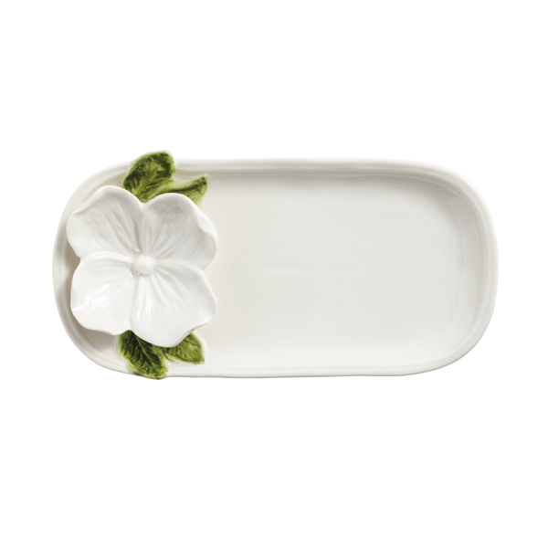 white ceramic tray with sculpted white flower and green leaves shown on a white background