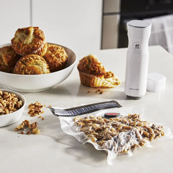 sealed vacuum bag filled with nuts set on a table with a bowl of muffins and a vacuum pump.