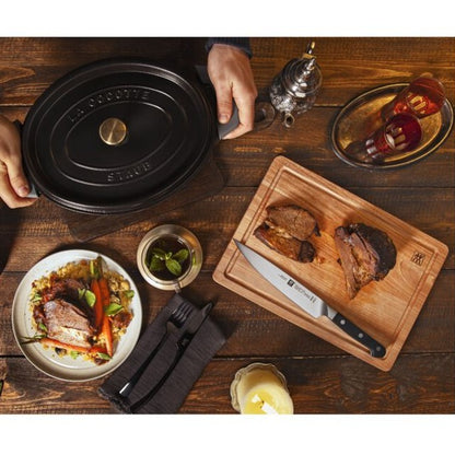 PRO 8 Inch Carving Knife laying on a cutting board with slices of meat and an array of dishes surrounding the board.