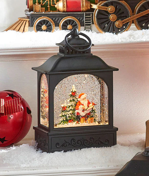 santa in the forest water lantern turned on and set on a table surrounded by artificial snow and a red bell.