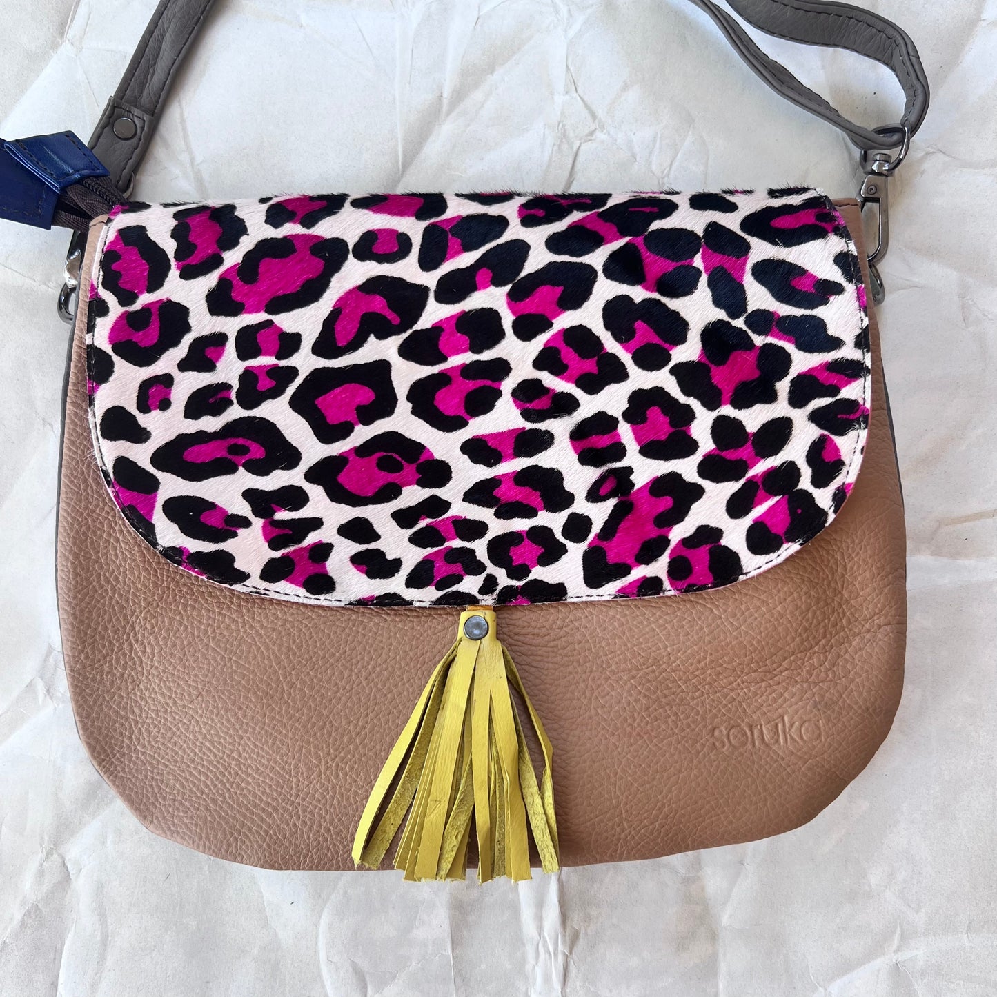 rounded brown purse with black and pink cheetah print flap, yellow tassel, and grey strap.