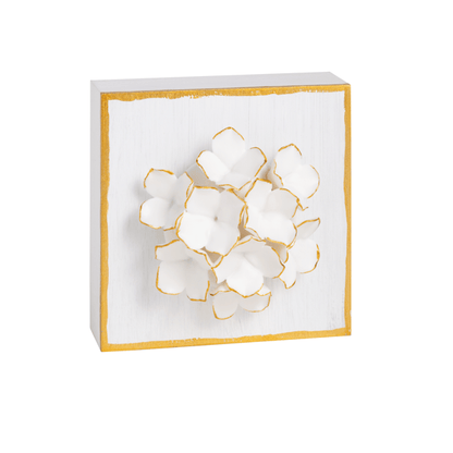 white wooden block edged in gold with white hydrangea-like flower on it, petals are trimmed in gold