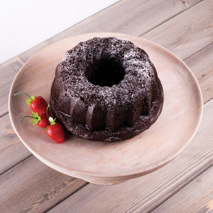 Chocolate bundt cake on a wooden plate with strawberries around it on a wooden surface