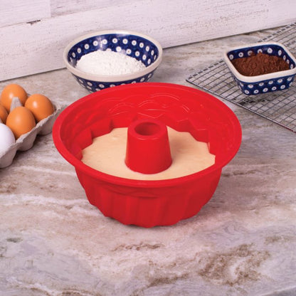 Red silicone bundt cake mold filled with batter on a kitchen counter with baking ingredients around it