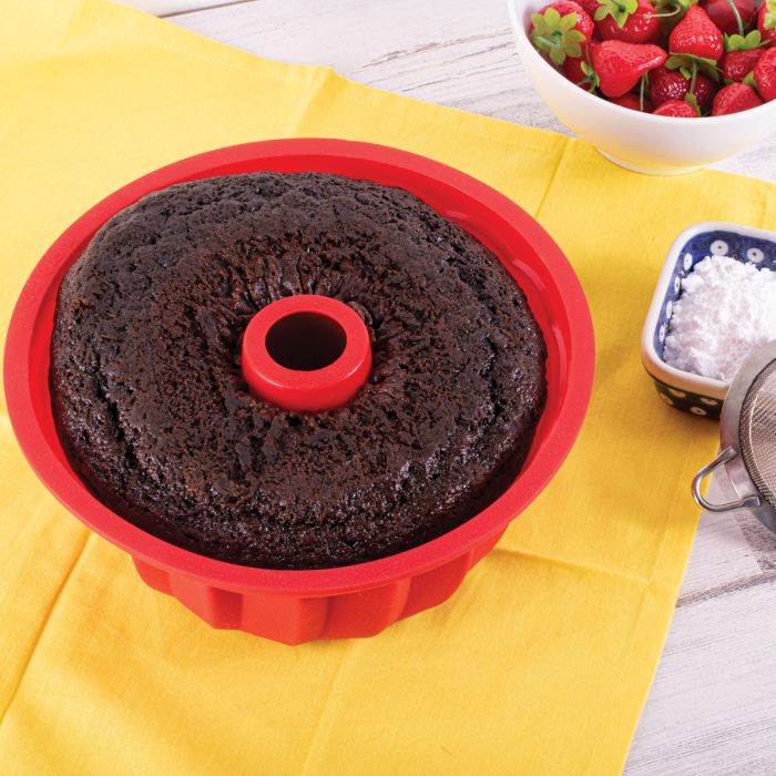 baked Chocolate cake in a red silicone bundt pan on a yellow tablecloth with strawberries in the background.
