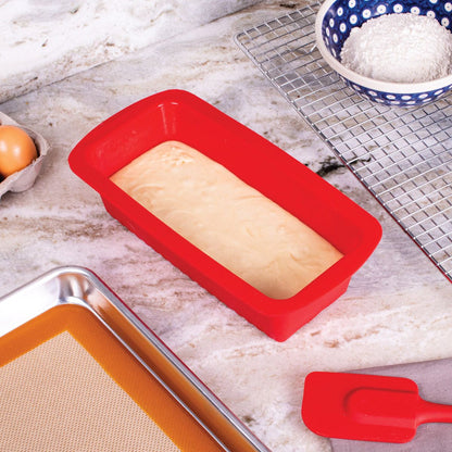 red silicone loaf pan filled with batter and set on a countertop with a cooling rack and baking ingredients.