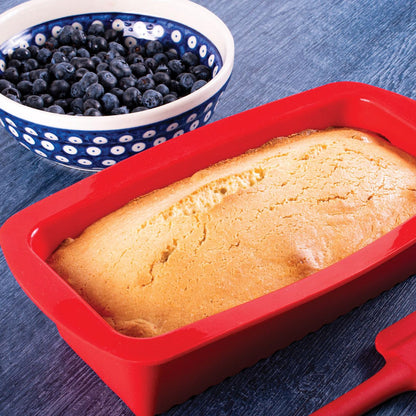 red silicone loaf pan filled with baked loaf set on a table with a bowl of blueberries.