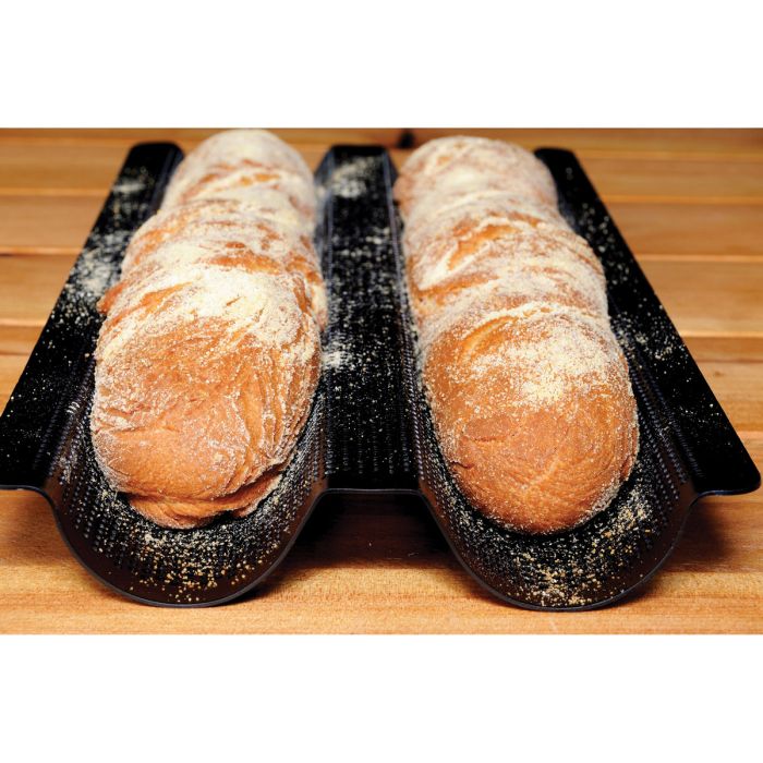 Two baked baguettes in a double baguette baking pan set on a wooden surface