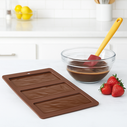 Chocolate mold on a kitchen counter with a bowl of chocolate mixture and strawberries.