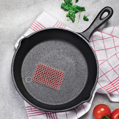 Chainmail Cast Iron Scrubber in a cast iron pan set on a dish towel on a countertop.