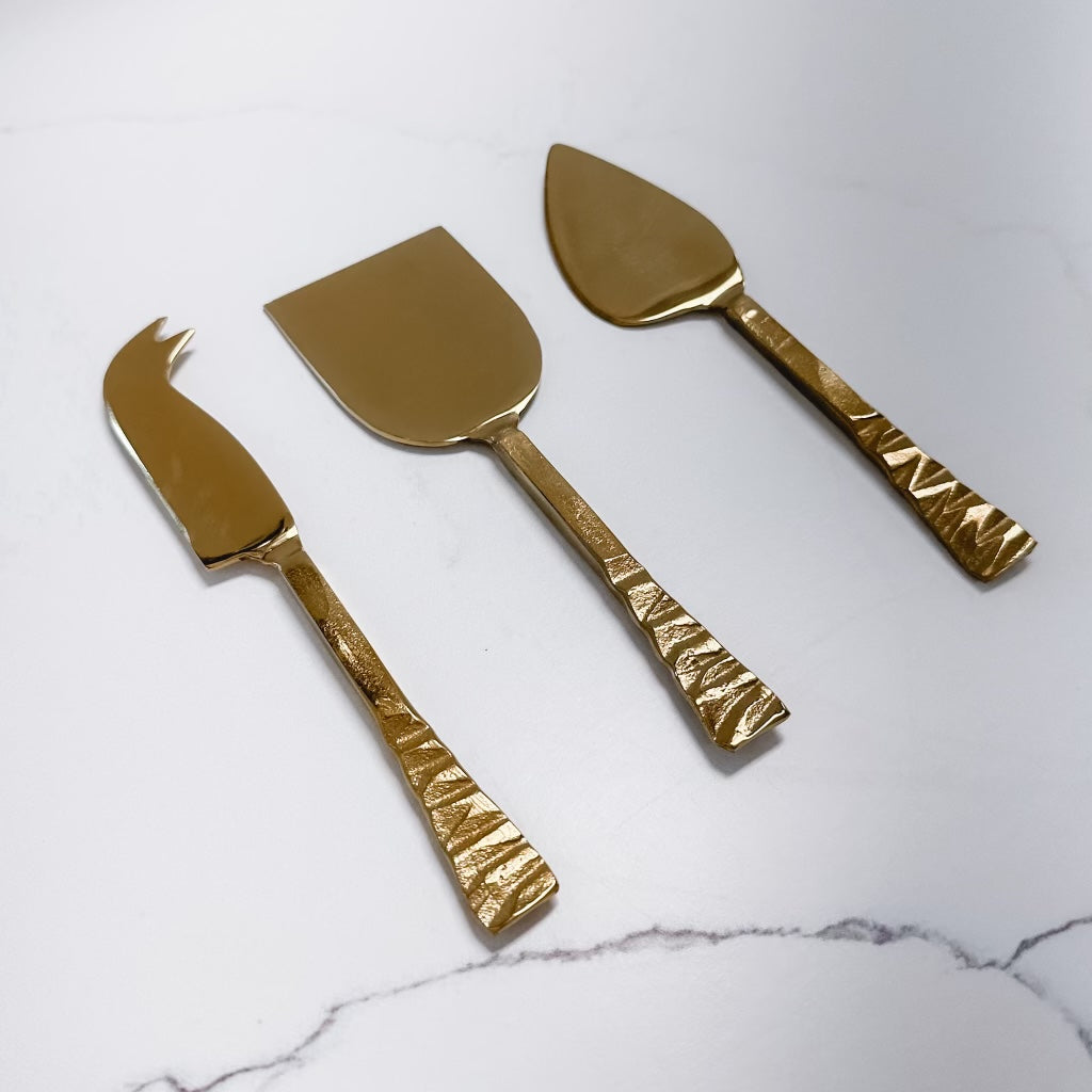 gold cheese knife, server, or fork with textured handles on a marble background.