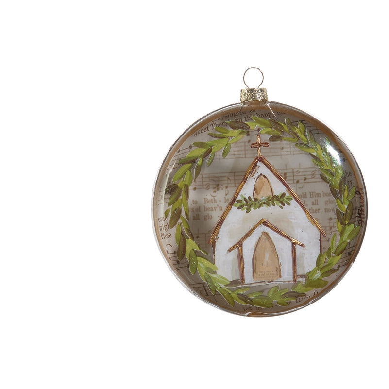 A round Christmas ornament featuring a painted white church with a green wreath, set against a background of vintage SHEET MUSIC