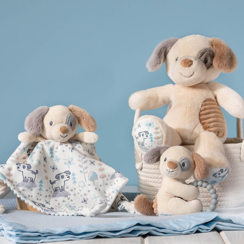 Puppy Soft Toy displayed on a basket next to the puppy lovey and puppy teether, all resting on a blue blanket