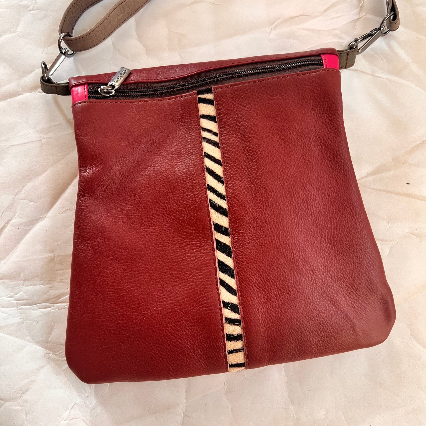 maroon greta bag with animal print stripe down the center and zipper at the top.