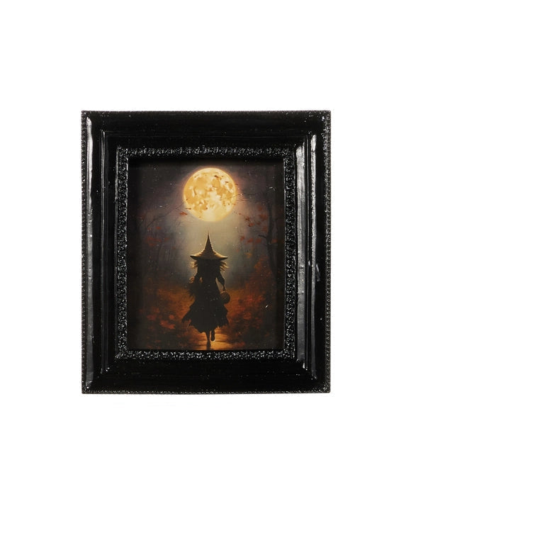 A framed art print depicting a witch's silhouette under a large, glowing full moon, set in a textured black frame against a plain white background.