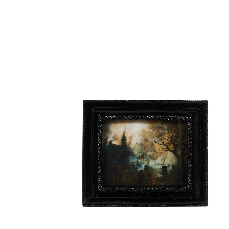 A small framed dark landscape painting depicting a spooky graveyard scene with a church steeple, bare trees, and tombstones, set in a black frame against a plain white background.