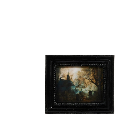 A small framed dark landscape painting depicting a spooky graveyard scene with a church steeple, bare trees, and tombstones, set in a black frame against a plain white background.