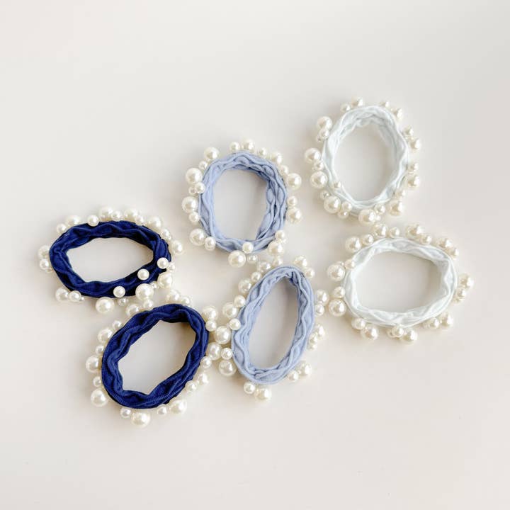 6 hair ties in white and 2 shades on blue all with pearls on them laying flat on a white background