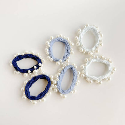 6 hair ties in white and 2 shades on blue all with pearls on them laying flat on a white background