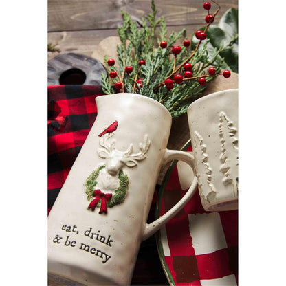 eat, drink and be merry deer pitcher laying in its side, filled with pine and berry sprigs, laying next to a christmas platter and buffalo checked towel