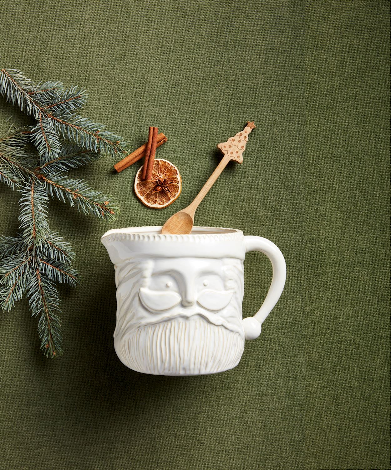 santa pitcher arranged on a green surface with evergreen sprigs and holiday spices.