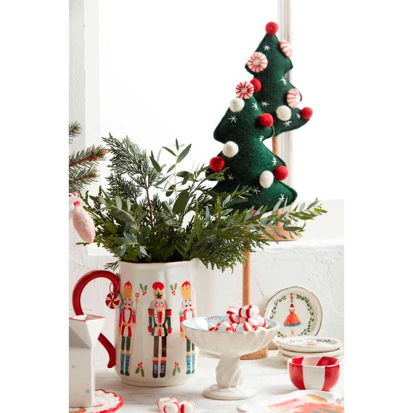 nutcracker pitcher filled with greenery and set on a table with other christmas dishes and decorations.