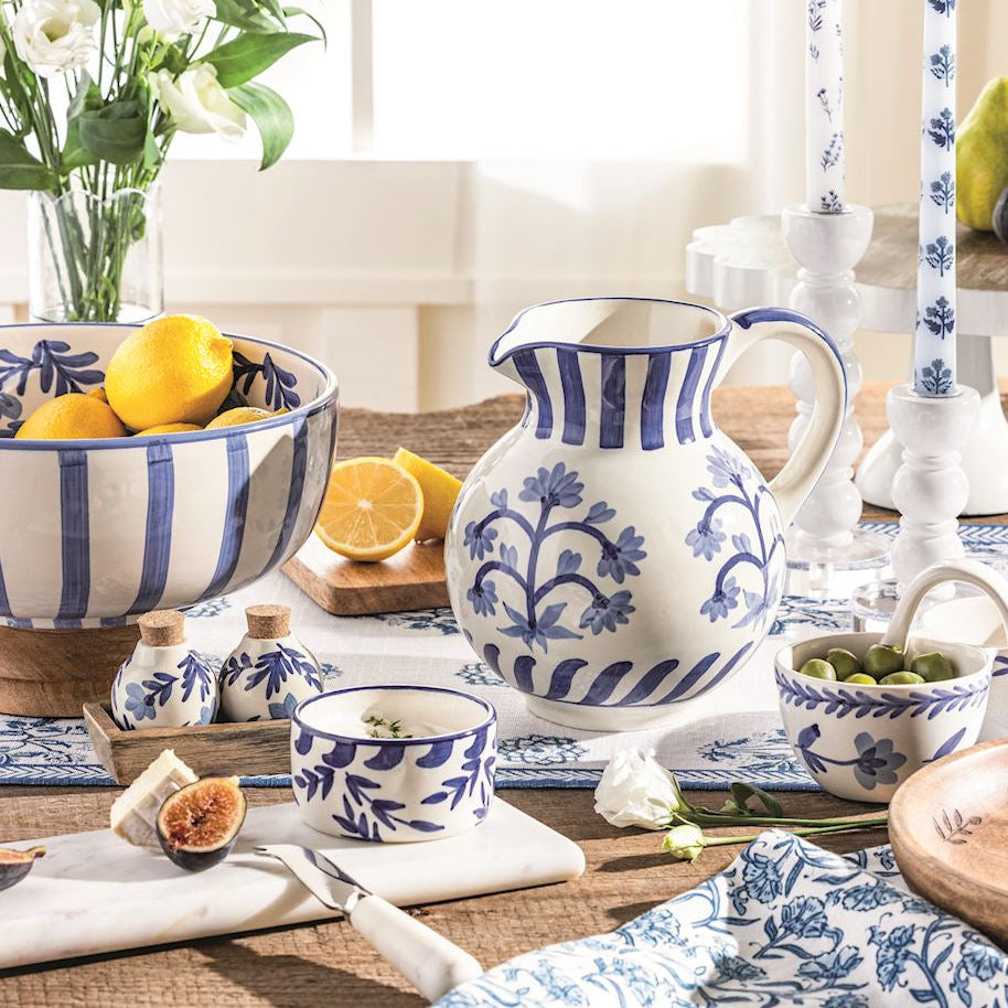 Table setting with blue and white ceramic bowl, pitcher and other dishes and fruits, and flowers.