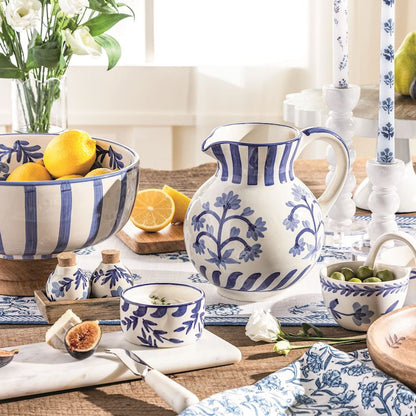 Table setting with blue and white ceramic bowl, pitcher and other dishes and fruits, and flowers.