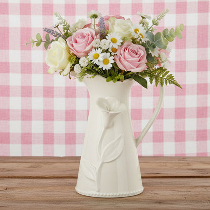White ceramic pitcher with floral design filled with spring flowers shown on a pink gingham background