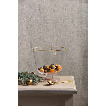 glass pedestaled bowl partially filled with fruit set on a table with gold spoon and holiday greenery.