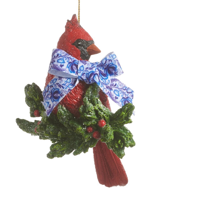 Christmas ornament shaped like a red cardinal perched on holly branch and a blue patterned bow on his neck