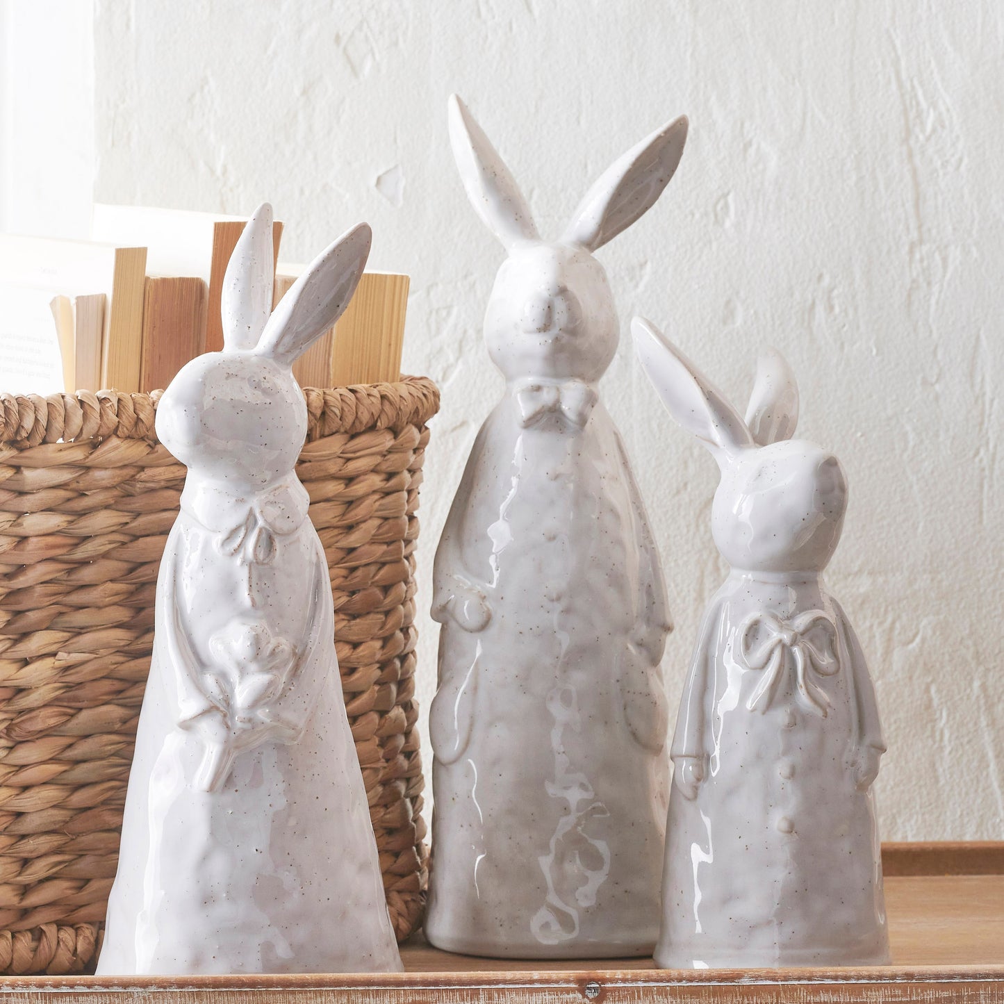 3 sizes of white ceramic rabbits arranged on a table with a basket